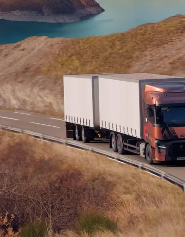 A Renault Trucks T tractor-trailer is traveling along a winding road overlooking a mountain lake.
