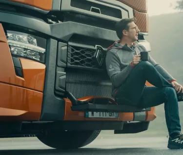 Model year 2025 : Renault Trucks T High Smart Racer : lifestyle (driver sitting on the windscreen access steps, relaxing with a cup in his hands)(Renault Trucks Stoneware Mug)(Renault Trucks Hero Zip Hoodie)